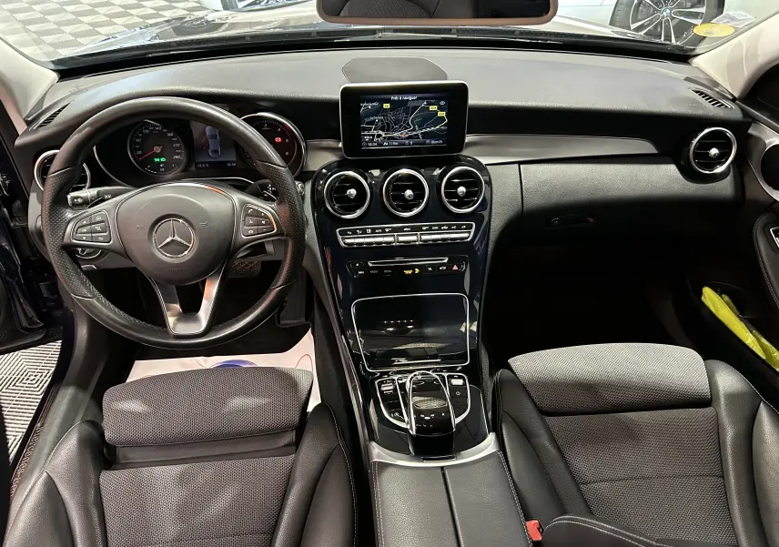 Vue intérieure avant de la Mercedes Classe C 200d bleu, mettant en valeur le tableau de bord et l'écran GPS central.