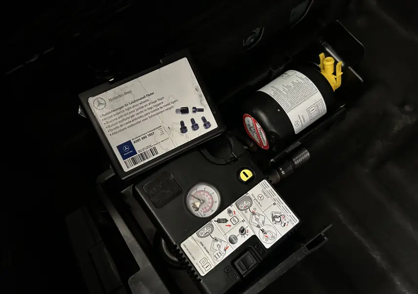 Gros plan sur le compresseur de roue et kit de réparation dans le coffre d'une Mercedes Classe C 200d bleu 2018.