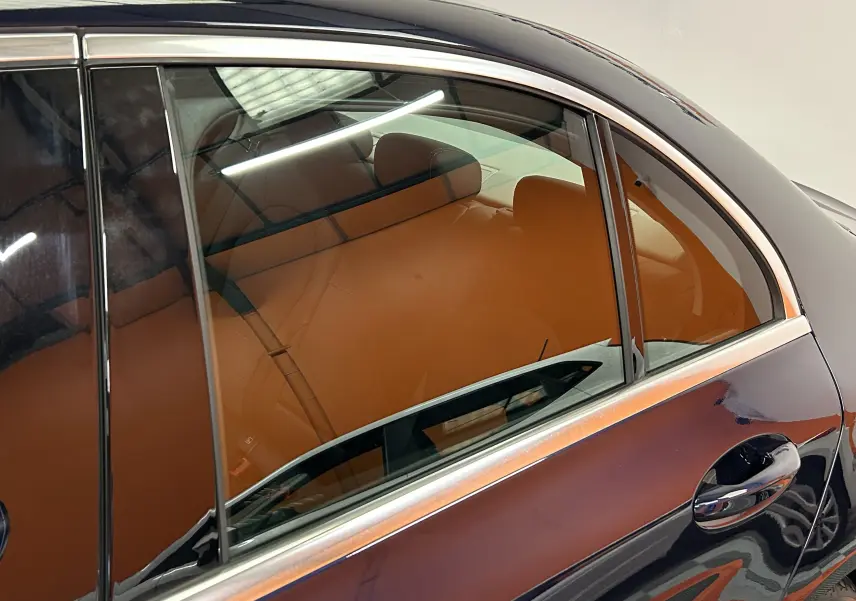 Vue latérale côté droit d'une Mercedes Classe C 200d bleu avec intérieur cuir marron visible à travers la vitre arrière.