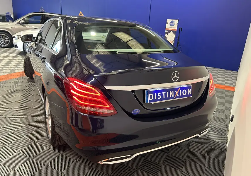 Vue 3/4 arrière d'une Mercedes Classe C 200d bleu foncé avec feux arrière allumés dans un showroom.