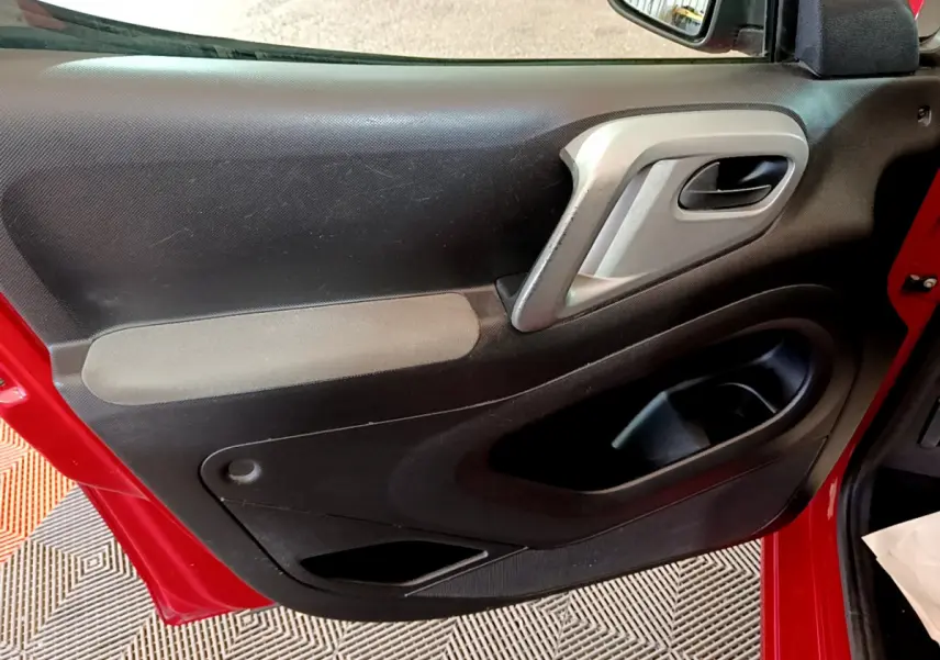Vue rapprochée de la porte avant gauche rouge du Citroën Berlingo 2016, montrant la poignée intérieure et les rangements.