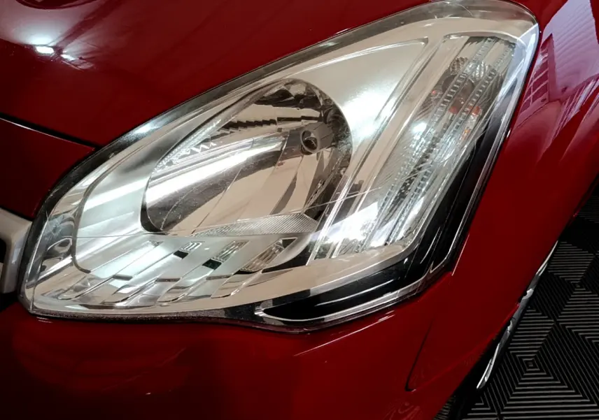 Gros plan sur le phare avant droit du Citroën Berlingo rouge, mettant en valeur son design et la carrosserie brillante.