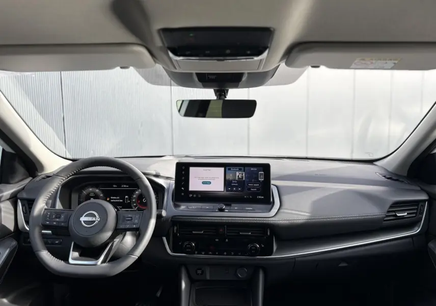 Vue frontale intérieure du Nissan Qashqai blanc nacré 2025, tableau de bord moderne avec écran tactile central et volant cuir.