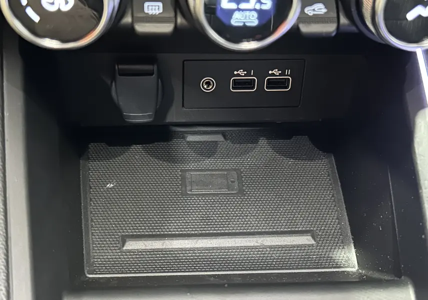 Gros plan sur la console centrale de la Renault Clio V E-Tech, montrant les ports USB et la zone de recharge sans fil.