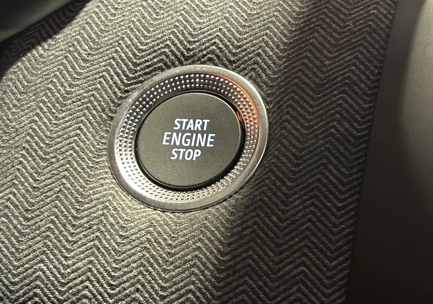 Bouton Start Engine Stop en gros plan sur le tableau de bord avec finition tissu à motif chevron de la Renault Clio V gris Rafale.