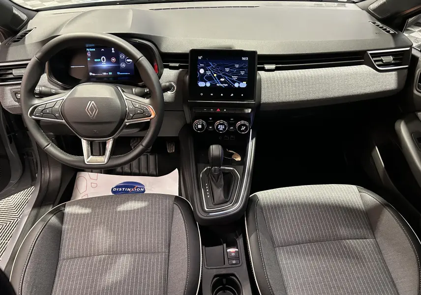 Vue intérieure avant de la Renault Clio V E-Tech avec tableau de bord gris, écran tactile GPS et sièges tissu gris rayé.