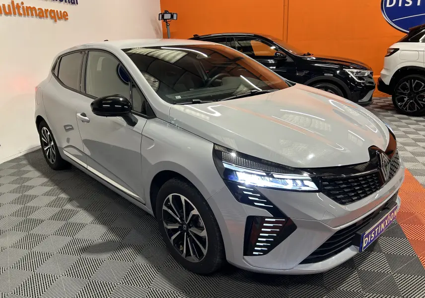 Renault Clio V E-Tech 145ch gris Rafale métal vue 3/4 avant avec feux LED allumés et jantes alliage.