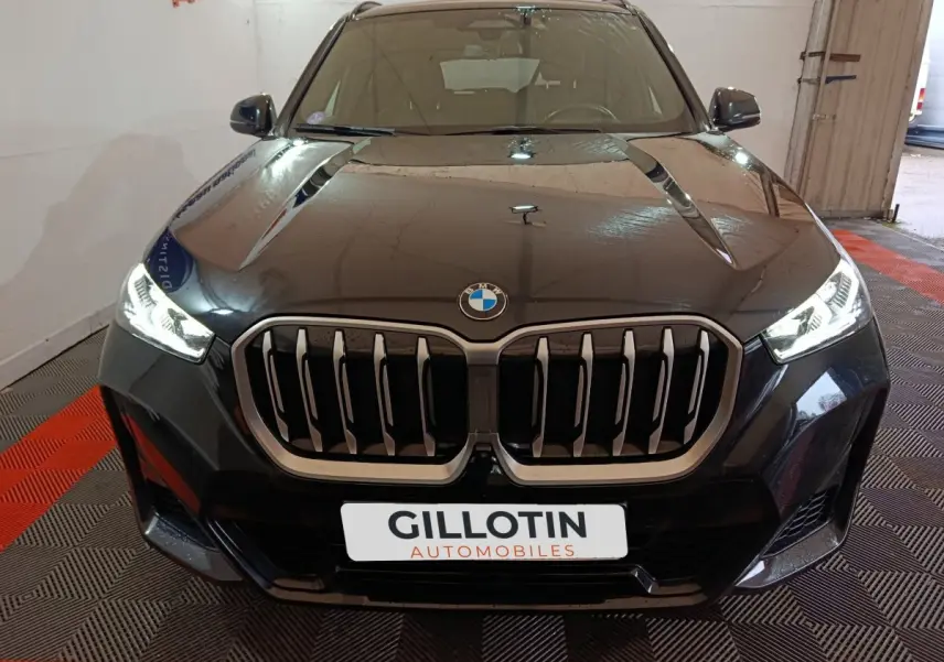 Vue avant rapprochée d’un BMW X1 noir avec calandre imposante et phares LED allumés dans un garage.