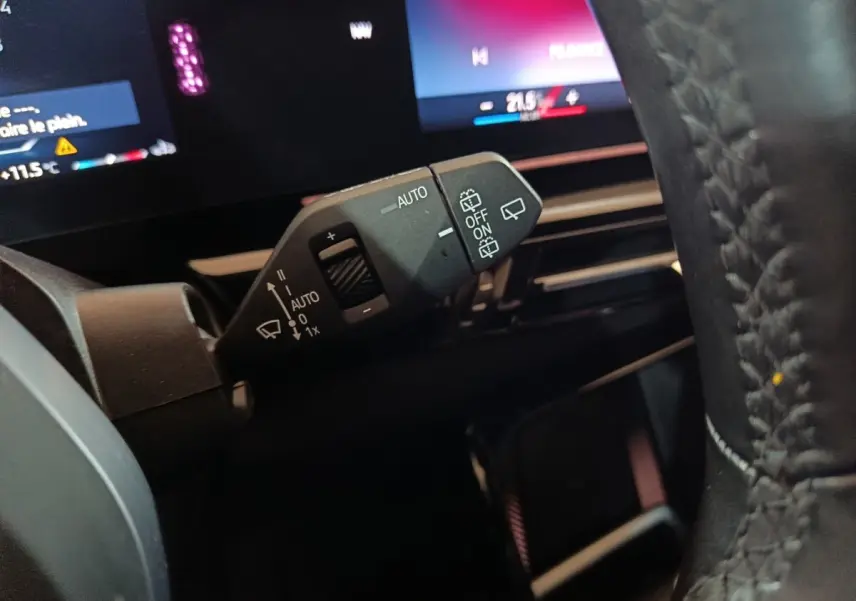 Gros plan sur la commande d’essuie-glace à gauche du volant en cuir d’un BMW X1 noir, tableau de bord digital en arrière-plan.