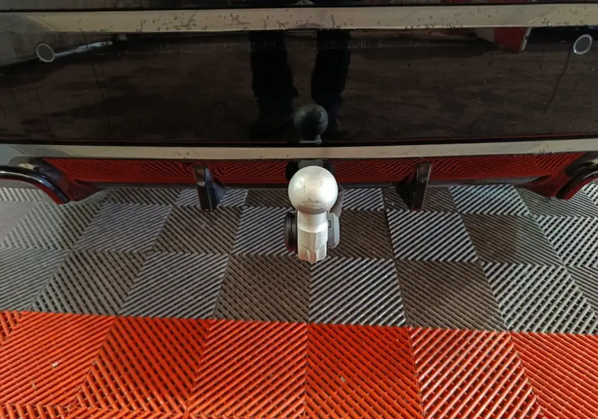 Gros plan sur l'attelage arrière d'un BMW X1 noir, mettant en valeur la boule d'attelage sur sol carrelé bicolore.