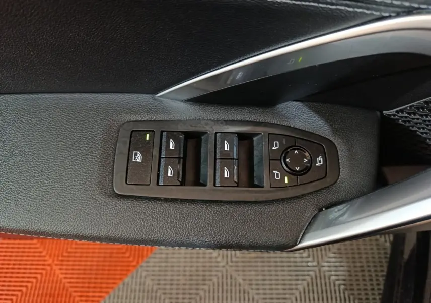 Gros plan sur les commandes de lève-vitres et rétroviseurs côté conducteur d’un BMW X1 noir, intérieur cuir noir.