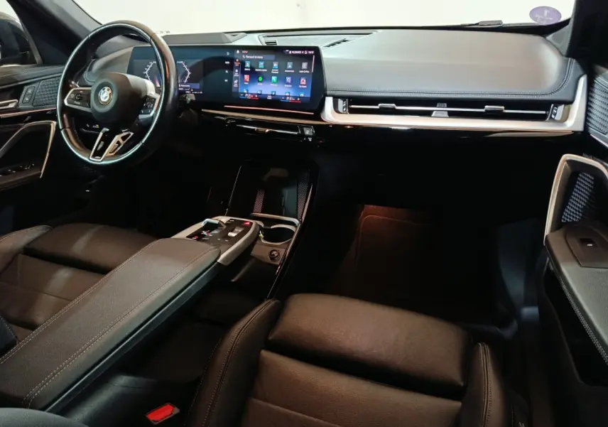 Intérieur noir BMW X1 xDrive23i M Sport 2023, vue de profil droit sur tableau de bord et volant cuir alu multifonctions.