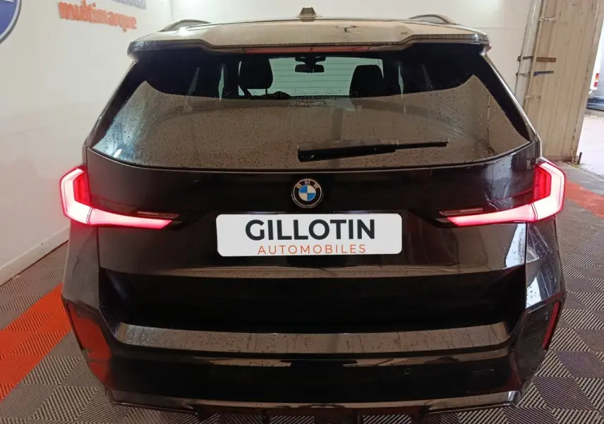 Vue arrière d’un BMW X1 noir avec feux arrière LED allumés dans un garage fermé.