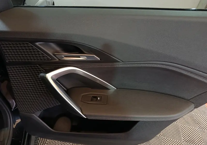 Gros plan sur la porte intérieure côté gauche du BMW X1 noir, avec poignée argentée et bouton de fenêtre électrique.