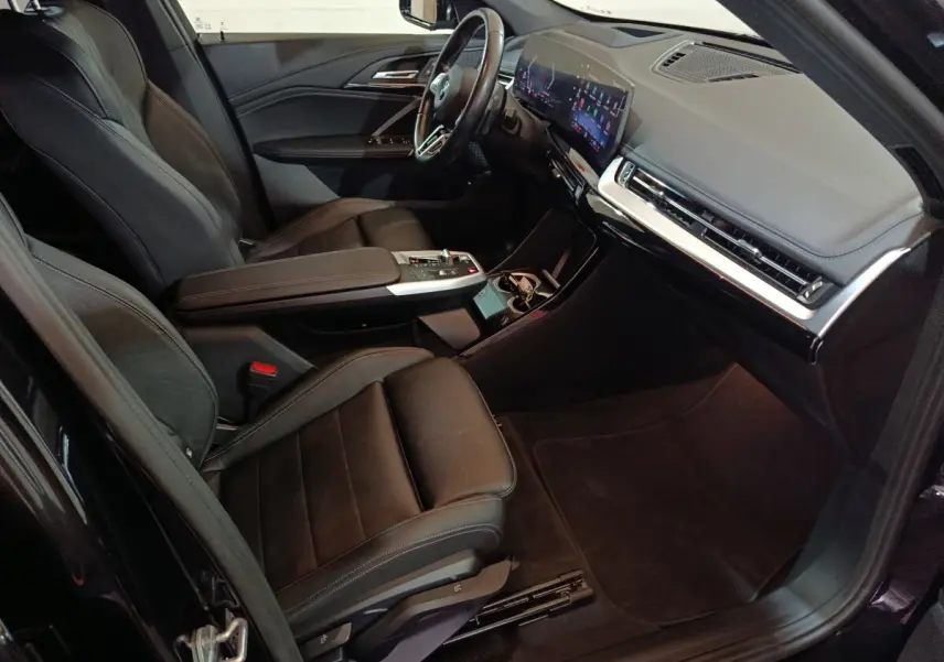 Vue intérieure côté conducteur de la BMW X1 xDrive23i M Sport 2023 avec sièges cuir noirs et écran tactile large.
