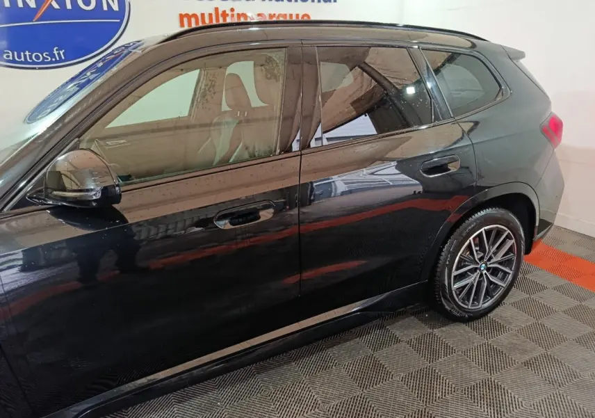 Vue de profil côté droit d'un BMW X1 noir 2023 avec jantes alliage et vitres teintées dans un showroom.