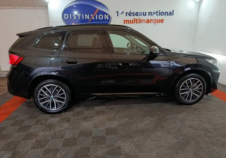 BMW X1 xDrive23i M Sport noir vue de profil côté gauche dans un showroom avec jantes alliage distinctives.