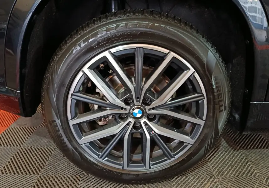 Gros plan sur la jante alliage noire et argentée avec logo BMW, montée sur pneu Pirelli All Season du BMW X1 noir.