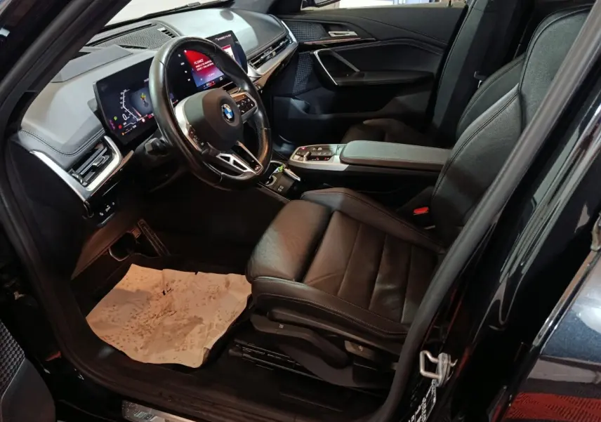 Vue intérieure côté conducteur du BMW X1 xDrive23i M Sport 2023 noir, avec tableau de bord digital et sièges cuir noirs.