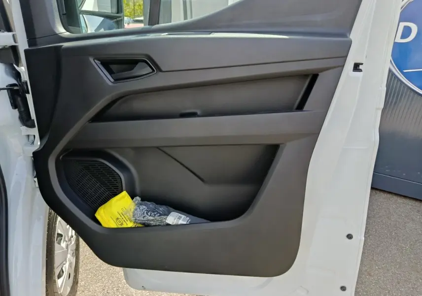 Vue rapprochée de la porte avant gauche noire du Renault Master blanc avec rangement contenant un objet jaune.