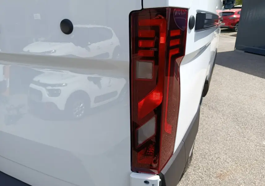 Gros plan sur le feu arrière droit du Renault Master blanc, avec reflet d’un autre véhicule sur la carrosserie.