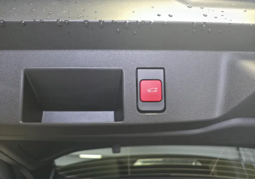 Détail du bouton rouge d'ouverture électrique du hayon sur le bord intérieur du coffre d'une Citroën C5 Aircross vert.