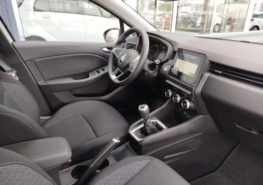 Vue intérieure côté conducteur de la Renault Clio V Business avec tableau de bord moderne et levier de vitesses manuel.