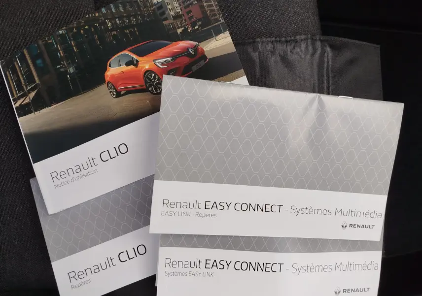 Brochures Renault Clio V avec une photo 3/4 avant d'une Clio orange vif en milieu urbain, sur fond noir.