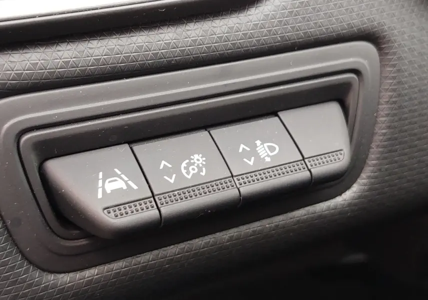 Gros plan sur les boutons de réglage d'assistance à la conduite et d'éclairage dans l'habitacle gris d'une Renault Clio V Business.