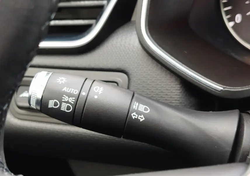 Gros plan sur la manette de commande des phares et clignotants du tableau de bord intérieur d'une Renault Clio V gris platine.
