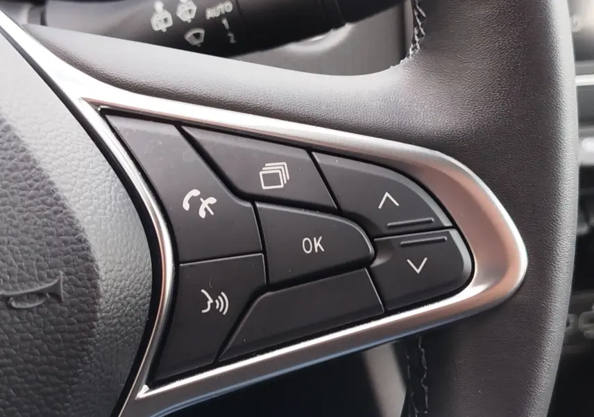Gros plan sur les commandes multifonctions noires et argentées du volant côté gauche d'une Renault Clio V gris platine.