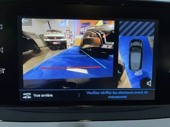 Affichage caméra de recul et vue 360° d'une Peugeot 208 rouge Elixir métal stationnée sur sol bleu en intérieur showroom.