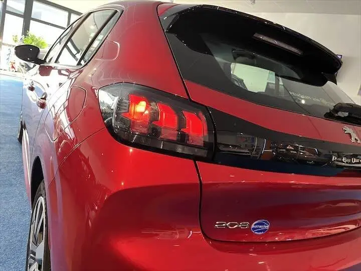 Vue arrière côté gauche d'une Peugeot 208 rouge Elixir Metal avec feux arrière allumés et badge distinctif sur le coffre.