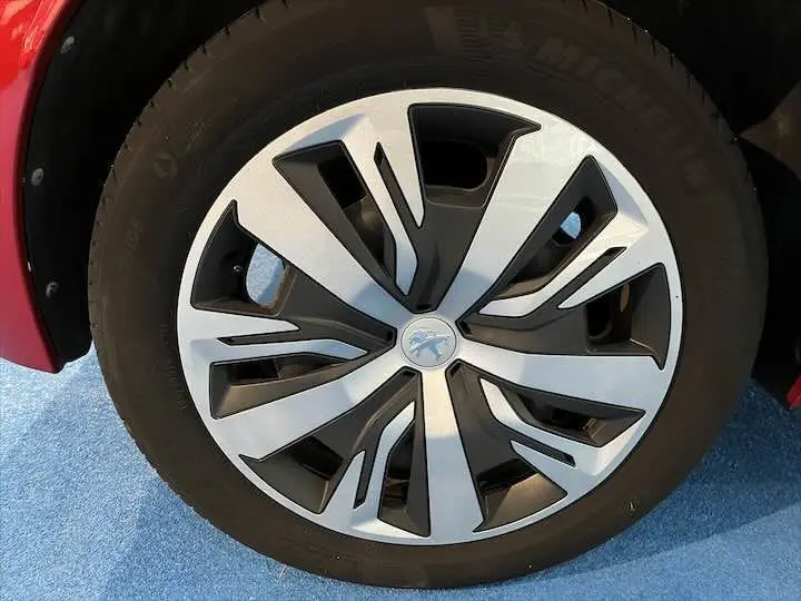 Gros plan sur la roue avant droite d'une Peugeot 208 rouge Elixir Metal avec jante en alliage au design moderne.