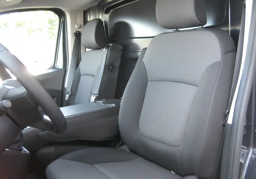 Vue intérieure du Renault Trafic Fourgon gris comète, montrant les sièges avant en tissu gris et le volant côté gauche.
