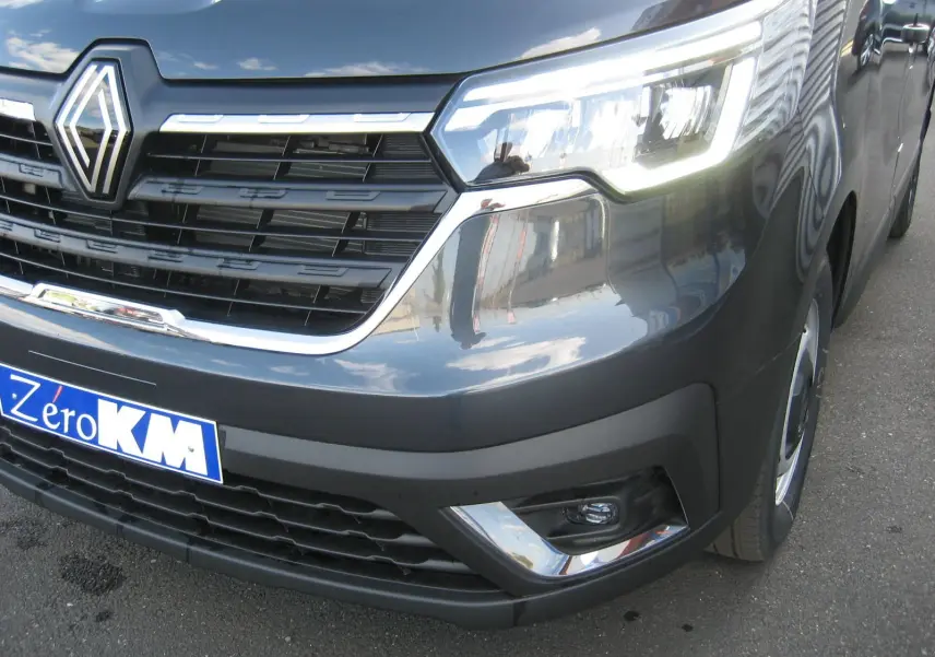 Gros plan sur l'avant droit du Renault Trafic Fourgon gris comète, mettant en valeur la calandre et les phares LED allumés.