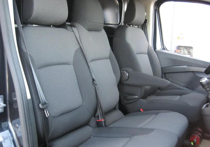 Intérieur du Renault Trafic Fourgon gris comète, vue latérale des sièges avant en tissu gris avec accoudoir côté droit.