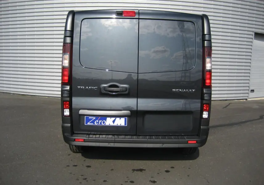 Vue arrière d'un Renault Trafic Fourgon gris comète avec portes battantes et plaque d'immatriculation Zero KM visible.