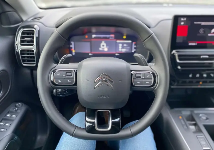 Vue intérieure centrée sur le volant noir du Citroën C5 Aircross 2025 avec tableau de bord numérique et écran tactile.