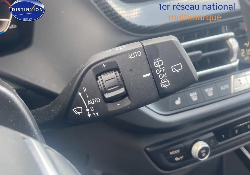 Gros plan sur la commande d’essuie-glace à gauche du volant d’une BMW Série 1 noire, tableau de bord en arrière-plan.