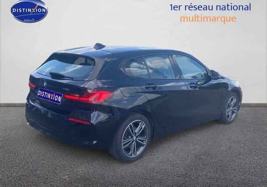 BMW Série 1 noire vue en 3/4 arrière droit, avec jantes alliage et feux arrière LED allumés.