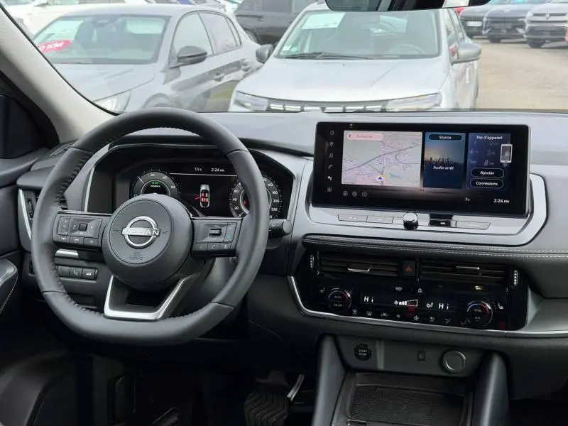 Vue intérieure avant du Nissan Qashqai Hybrid e-POWER 2025, tableau de bord noir avec écran tactile et volant multifonction.