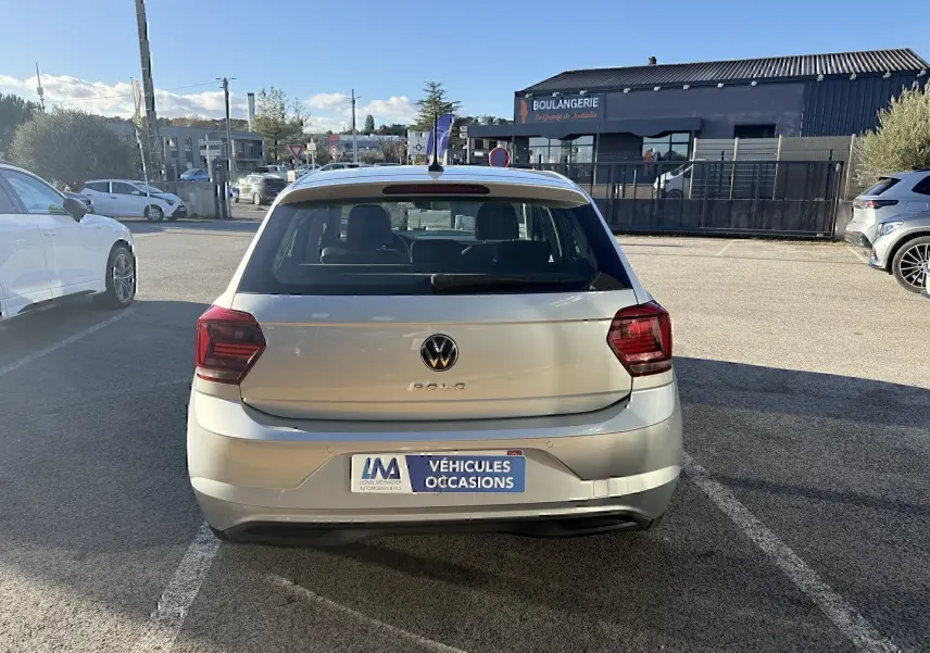 Vue arrière d'une Volkswagen Polo gris métal 2021 garée sur un parking en plein jour avec plaque "Véhicules Occasions".