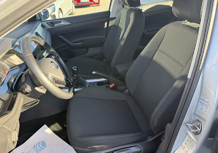 Vue intérieure côté conducteur de la Volkswagen Polo gris métal 2021, montrant sièges noirs et volant avec boîte manuelle.