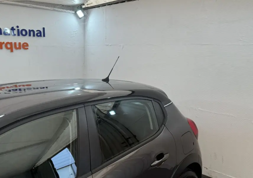 Vue 3/4 arrière droit d'une Citroën C3 gris foncé avec antenne sur le toit dans un garage blanc.