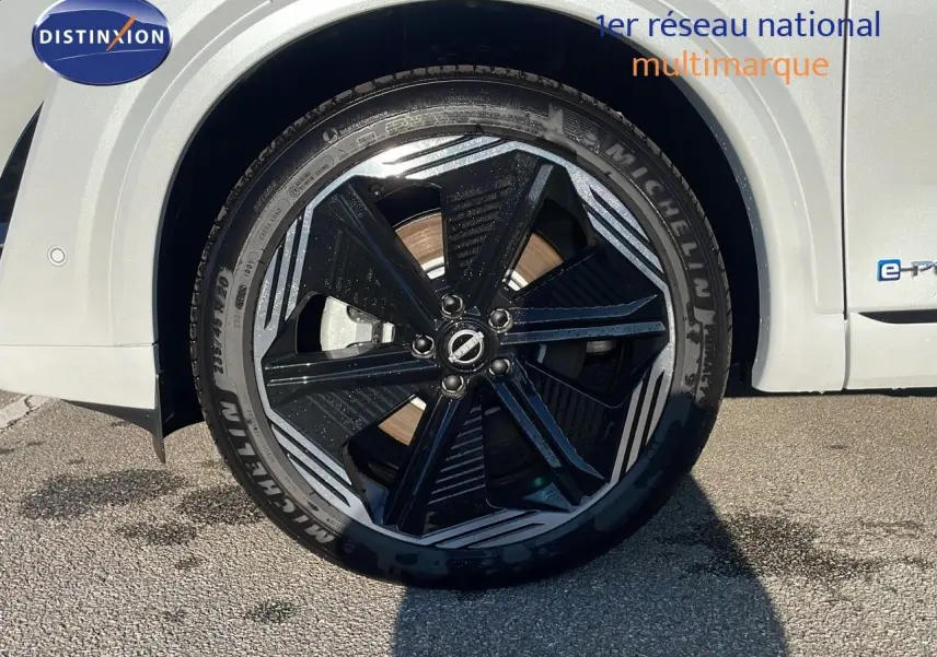 Gros plan sur la roue avant gauche du Nissan Qashqai blanc nacré avec jante noire et détails gris métallisé.