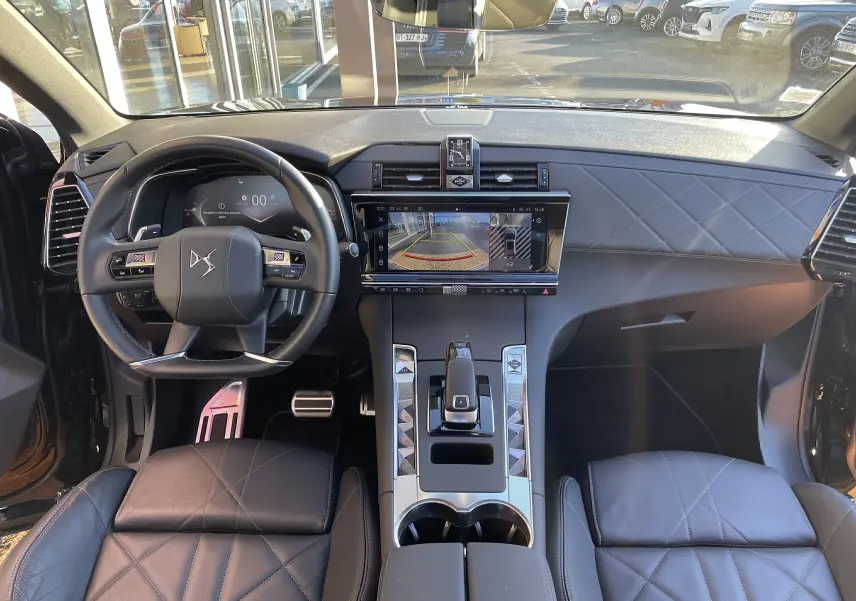 Vue intérieure avant du DS7 2024 noir Perla Nera, volant cuir, écran central affichant la caméra de recul et tableau de bord digital.