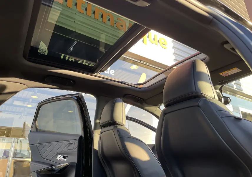 Intérieur du DS7 2024 noir Perla Nera, vue arrière côté gauche avec toit ouvrant panoramique et sièges cuir noir.