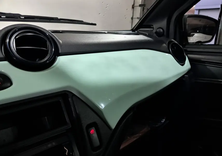 Tableau de bord vert clair vu côté passager de l'AIXAM MINAUTO E chic 2025 avec aérateurs ronds noirs et rétroviseur caméra côté conducteur visible.