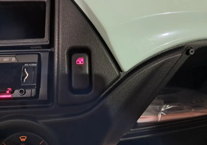 Gros plan sur l'intérieur de l'AIXAM MINAUTO E chic 2025, montrant un bouton de verrouillage de porte illuminé en rouge sur tableau de bord vert.